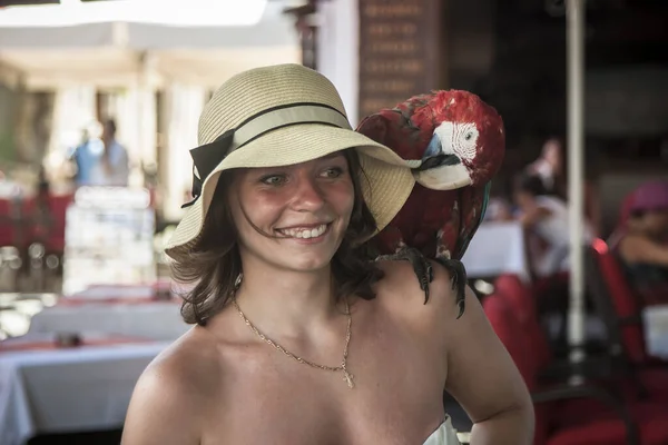 Arara Vermelha Senta Ombro Uma Menina Rindo Morde Pelo Chapéu — Fotografia de Stock