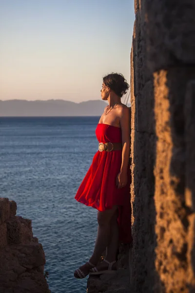 Dívka Červených Šatech Stojí Kamenné Zdi Obdivuje Moře — Stock fotografie