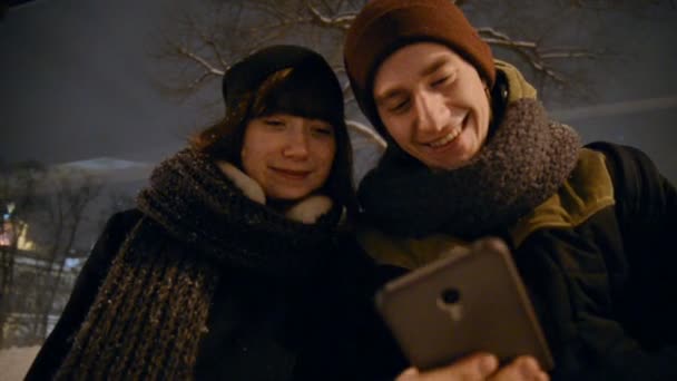 Junger Mann und Frau mit Touchpad auf nächtlichem Stadtbusbahnhof, informationsgeleitetem Display und Menschen, die im Hintergrund in den Bus steigen — Stockvideo