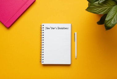 Stock photo of new year notebook with list of resolutions and objects on yellow background clipart