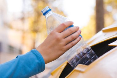 Plastik bir şişeyi geri dönüştüren bir kadının el resmi.