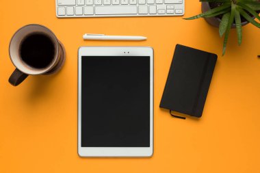 Siyah defterli beyaz bir tablet ve sarı arka planda beyaz bir kalem.