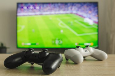 Bir masada iki oyun bloknotunun resmi ve arka planda bir futbol maçı.