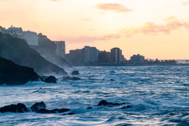 Ufukta Puerto de la Cruz binalarıyla Tenerife adasının kuzey sahilindeki El Bollullo sahilinden görülebilen puslu gün batımı.