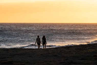 Tenerife, İspanya - 22 Aralık 2019: Gün batımında Tenerife 'deki la Tejita plajında yürüyen genç bir çiftin silüetleri.
