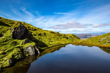 Scottish Highlands summer landscape with a deep blue sky and rocks reflecting reflecting in a little pond near the peak of Meall nan Tarmachan. Perthshire, Scotland.