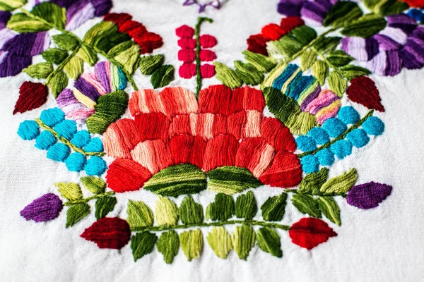 Close-up on a traditional Mexican women\'s blouse with colorful embroidered floral motif.