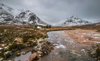 Glen Coe 'nun resimli kış manzarası. Buachaille Etive Mor' un eteklerinde ikonik beyaz kır evi, ufukta fırtınalı bulutlar..