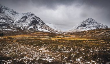 Glen Coe, İskoçya 'nın kış manzarası, Buachaille' in karlı zirveleri Etive Beag ve Aonach Eagach ufukta fırtınalı bulutlar.