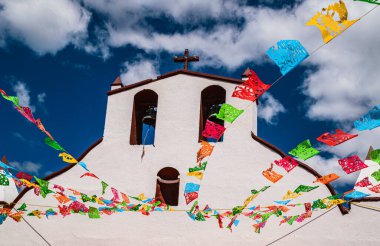 Meksika, Chiapas kırsalında küçük beyaz bir kiliseye yukarıdan bir perspektif, derin mavi gökyüzü zeminine karşı renkli bayraklar.