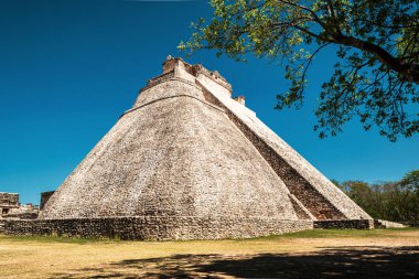Uxmal, Yucatn, Meksika 'nın antik Maya şehrindeki Sihirbaz Piramidi' nin yan görüntüsü derin mavi gökyüzünün arka planına karşı.