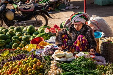 Loikaw, Myanmar - 29 Ocak 2018: Birmanyalı kadın geleneksel kıyafetler giyiyor ve Thanaka 'nın boyalı yüzü pazarında taze ürünler satıyor.. 