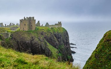 Dunnottar Kalesi, sisli ve yağmurlu bir yaz gününde İskoçya, Aberdeenshire 'ın kayalıklarına tünedi..