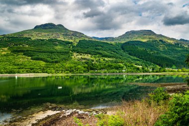 Arrochar Alplerinin yeşil tepeleri Loch Long 'u yansıtıyor. Güzel İskoç Highlands yaz manzarası bulutlu bir günde.