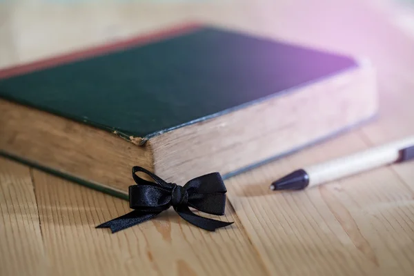 Чорний лук зі стрічкою зі старою книгою на столі, розмитим і м'яким світлом — стокове фото