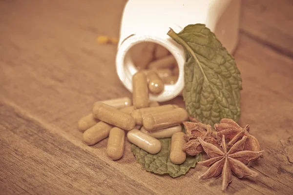 Hoja de menta y cápsula de hierba que se derrama de una botella — Foto de Stock