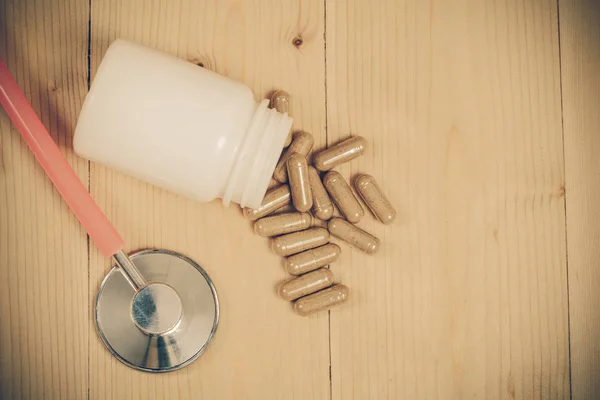 Herb capsules and stethoscope on wood table — Stock Photo, Image