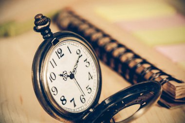 ahşap arka plan üzerinde kitap notalı cep saati.