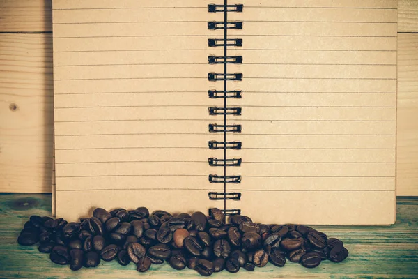 Coffee beans and note book on wooden table,still — Stock Photo, Image