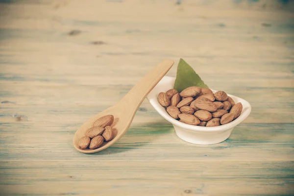 Almonds in bowl on wood and oil bottle — Stock Photo, Image