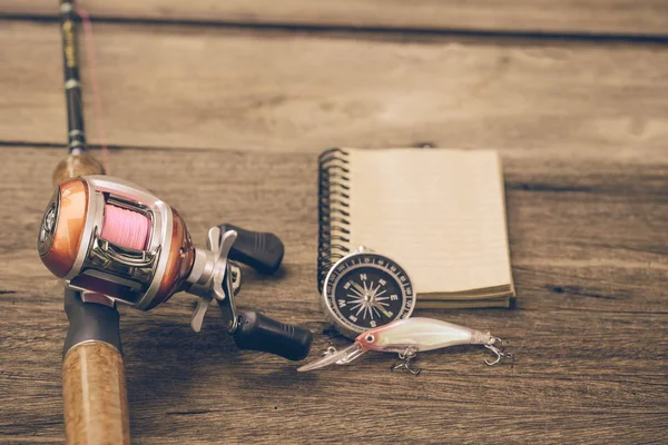 Fishing tackle - Baitcasting Reel, book and compass on  wooden b — Stock Photo, Image