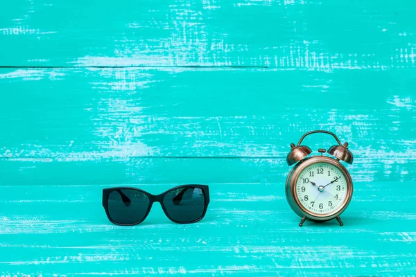Old alarm clock and sunglasses on color wood background — Stock Photo, Image