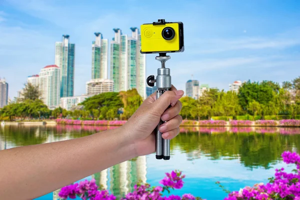 Action camera in hand to take a movie in city background.