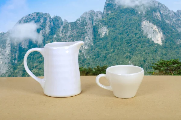 Copo de café branco e frasco na mesa de madeira com fundo da natureza . — Fotografia de Stock