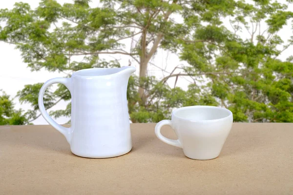 Weiße Kaffeetasse und Glas auf Holztisch mit Naturhintergrund. — Stockfoto