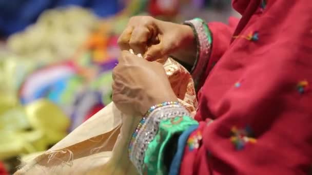 An elderly Arab woman in traditional colorful clothes sews local clothes — Stock Video