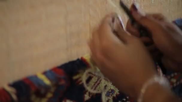 Eine Frau näht einen orientalischen Teppich. Hände arbeiten in Nahaufnahme hinter einem Webstuhl — Stockvideo