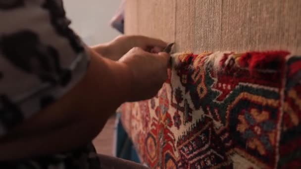 An elderly woman sews an oriental carpet. Close-up of hands work behind a loom — Stock Video