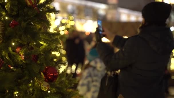 Menina não identificável fotografa uma árvore de Natal. Vista através da árvore de Ano Novo — Vídeo de Stock