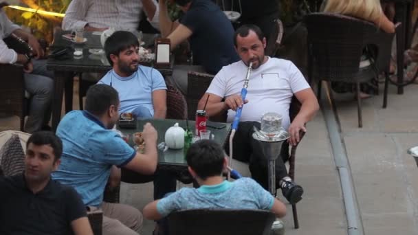 A company of Muslim is resting at a table in a street cafe. One smokes a hookah. — 비디오