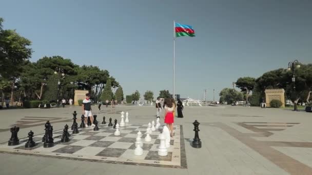Stadsplein met enorme schaakstukken. Tieners in kleurrijke kleren spelen schaak — Stockvideo