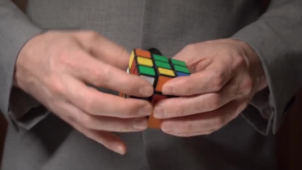 Man i jacka försöker samla färgerna på en rubiks kub. Pusselspel — Stockvideo