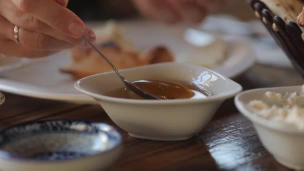 Una mujer recoge miel con una cuchara y se extiende sobre la tortilla oriental con queso — Vídeo de stock