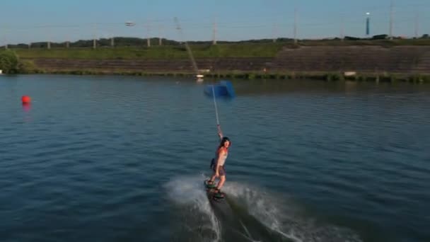 Garota wakeboarder montando a água do lago. Tiro aéreo de um teleférico em um lago . — Vídeo de Stock