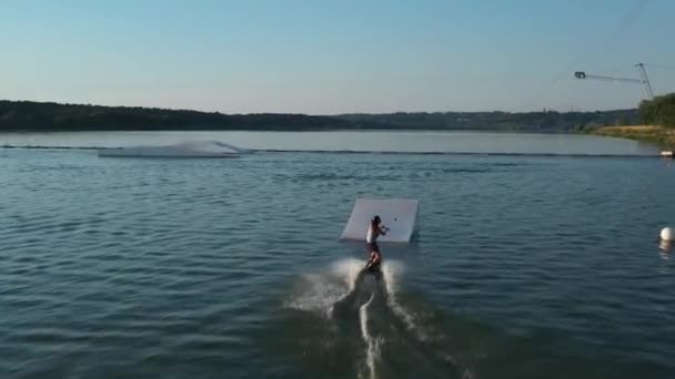 Garota wakeboarder montando a água do lago. Tiro aéreo de um teleférico em um lago . — Vídeo de Stock