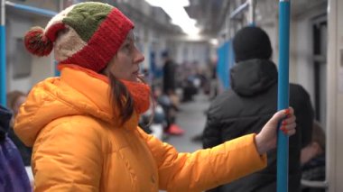 Kışın giyinmiş bir kadın tren vagonuna biner ve korkuluklara tutunur.