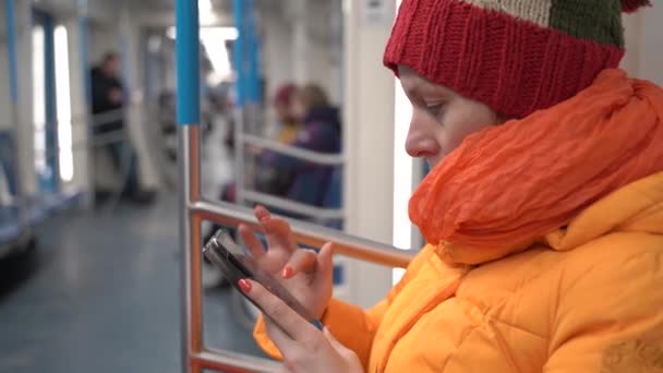 Una mujer está sentada en el metro con un teléfono móvil. Ella lee algo. — Vídeos de Stock