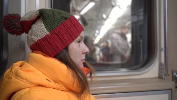 Una mujer en ropa de invierno monta en un vagón de tren y se sienta pensativamente . — Vídeo de stock