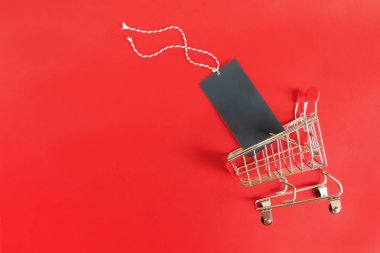 Kırmızı arka planda boş siyah etiketli küçük süpermarket arabası. Satış, Kara Cuma, siber pazartesi, online alışveriş konsepti..