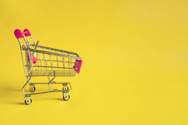 Sarı arka planda pembe saplı boş bir alışveriş arabası. İnternetten alışveriş konsepti. Bir çeşit elektronik ticaret..