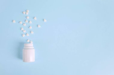 Şişeden kalp sızan beyaz haplar mavi arka planda izole edilmiş ve metin için kopyalanmış. Tıbbi konsept - üst görünüm. Alternatif Homeopati ilaç şifalı bitkiler, sağlık sigortası ve hap konsepti.