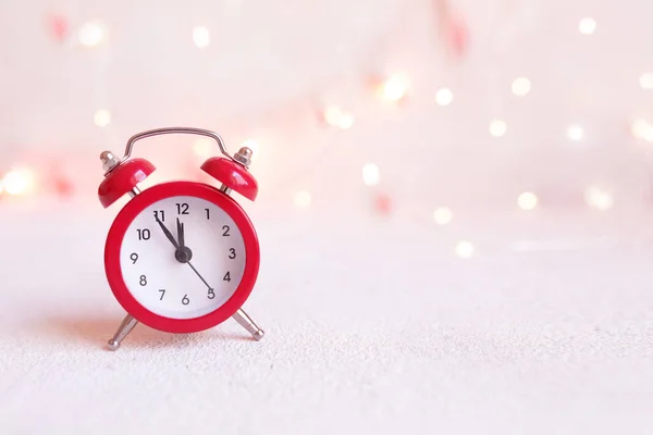Countdown to midnight. Red clock on a background of sparkling golden lights of a garland. Retro style clock counting last moments before Christmass or New Year.