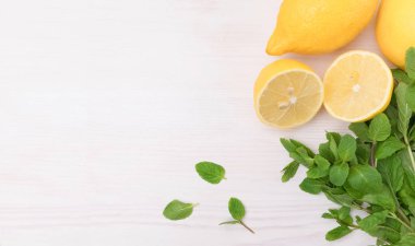 Banner of lemon and fresh mint leaves on a light wooden background. Mint and lemon for dessert and drinks. Yellow sliced lemon on wooden board with copy space.