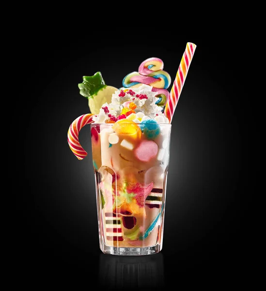 Monster shake, freak caramel shake isolated. Colourful, festive milk shake cocktail with sweets, jelly. Colored caramel milkshake array of different childs sweets and treats in glass on black