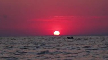 Kırmızı altın saat ve güneş ufkun ötesinde kayboluyor, küçük bir tekne geçiyor..