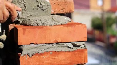 İşçinin eli kırmızı tuğlaya beton döşüyordu. Bir evin duvarına..